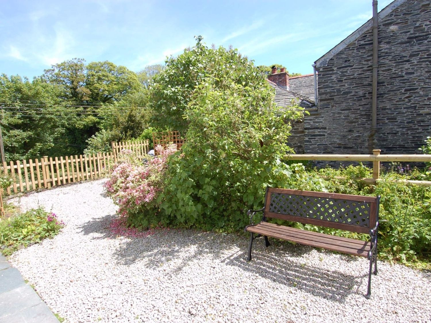 A garden area with a wooden bench gravel path flowering bushes and stone building at Jordan House in Boscastle