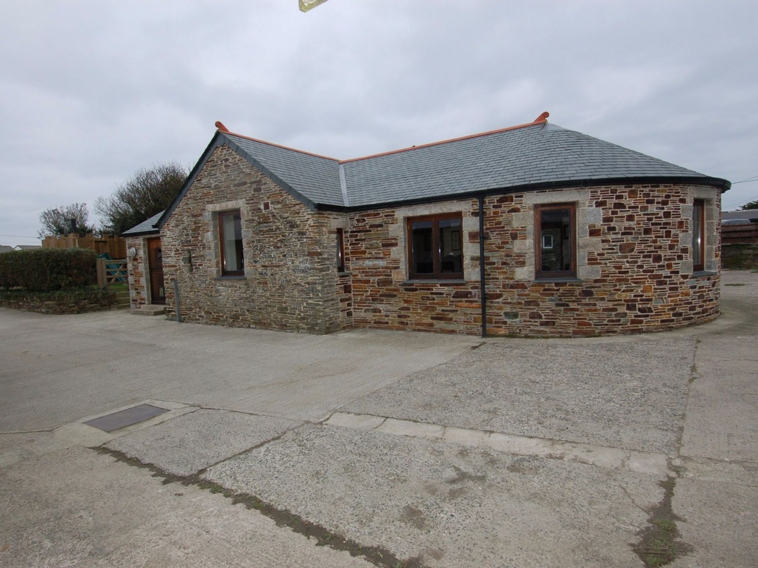 A single story stone house with multiple windows and a gray roof on a concrete driveway at Hideaway in Tintagel