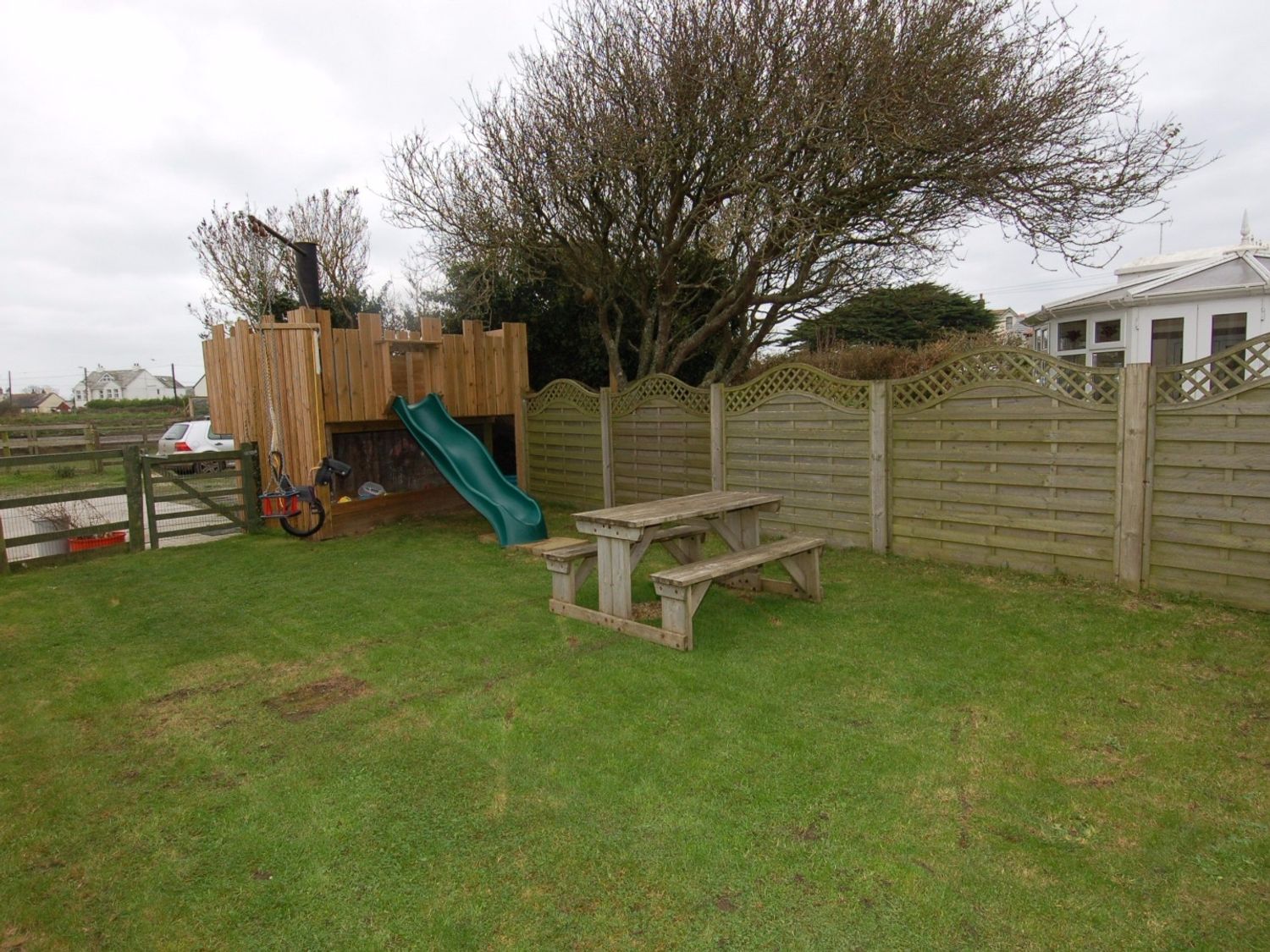 A backyard with a wooden play structure with a green slide a swing and a picnic table on grass at Hideaway in Tintagel