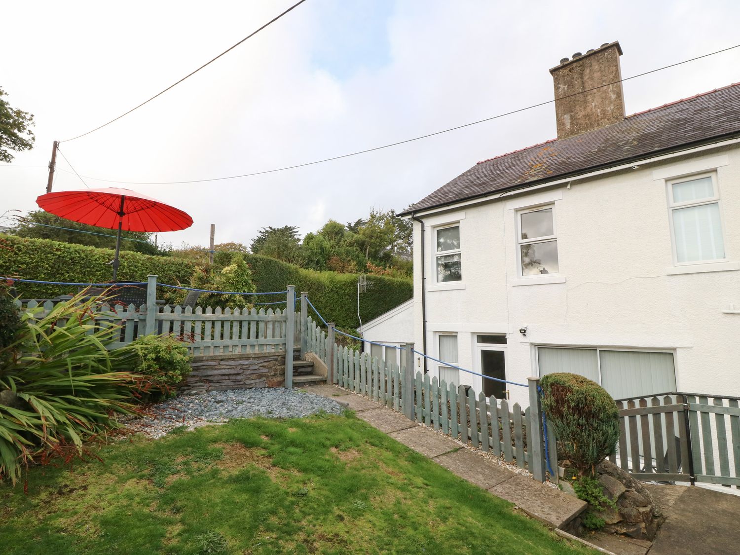 An outdoor area with a green picket fence and steps leading to a patio with a red umbrella at 2 Argoed in Llanbedrog