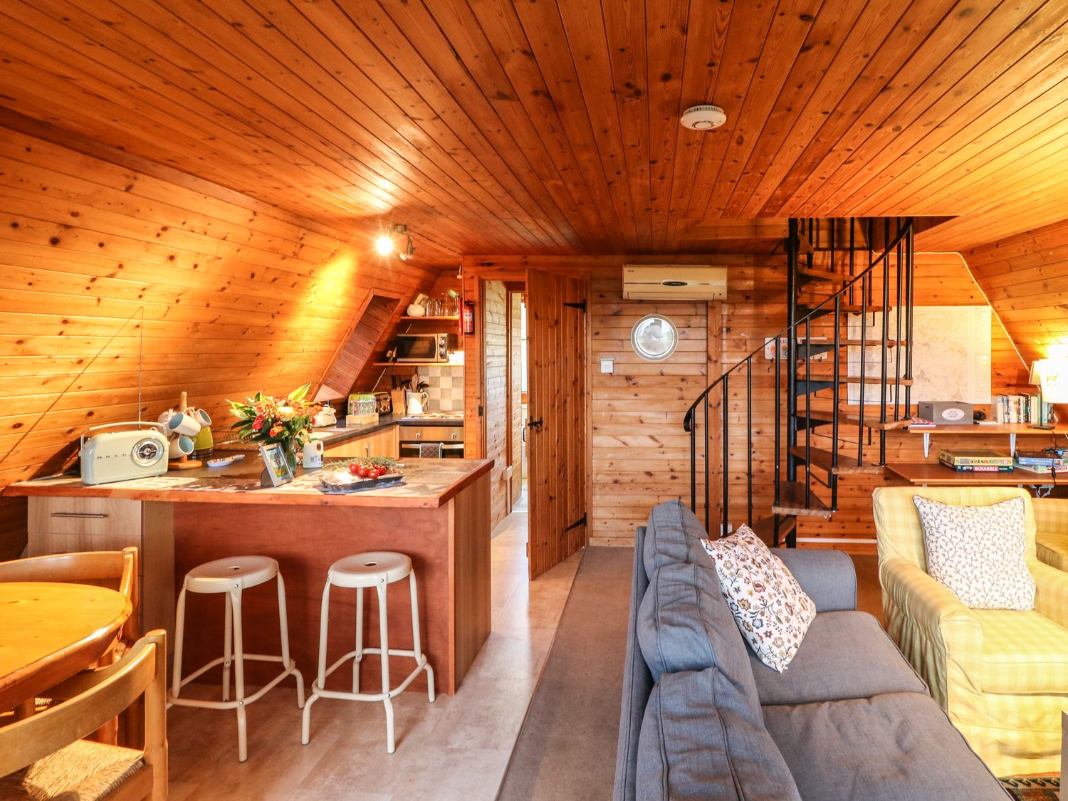 A wooden interior living area with kitchen island stools spiral staircase and seating at Rose Lodge in Milton on Stour