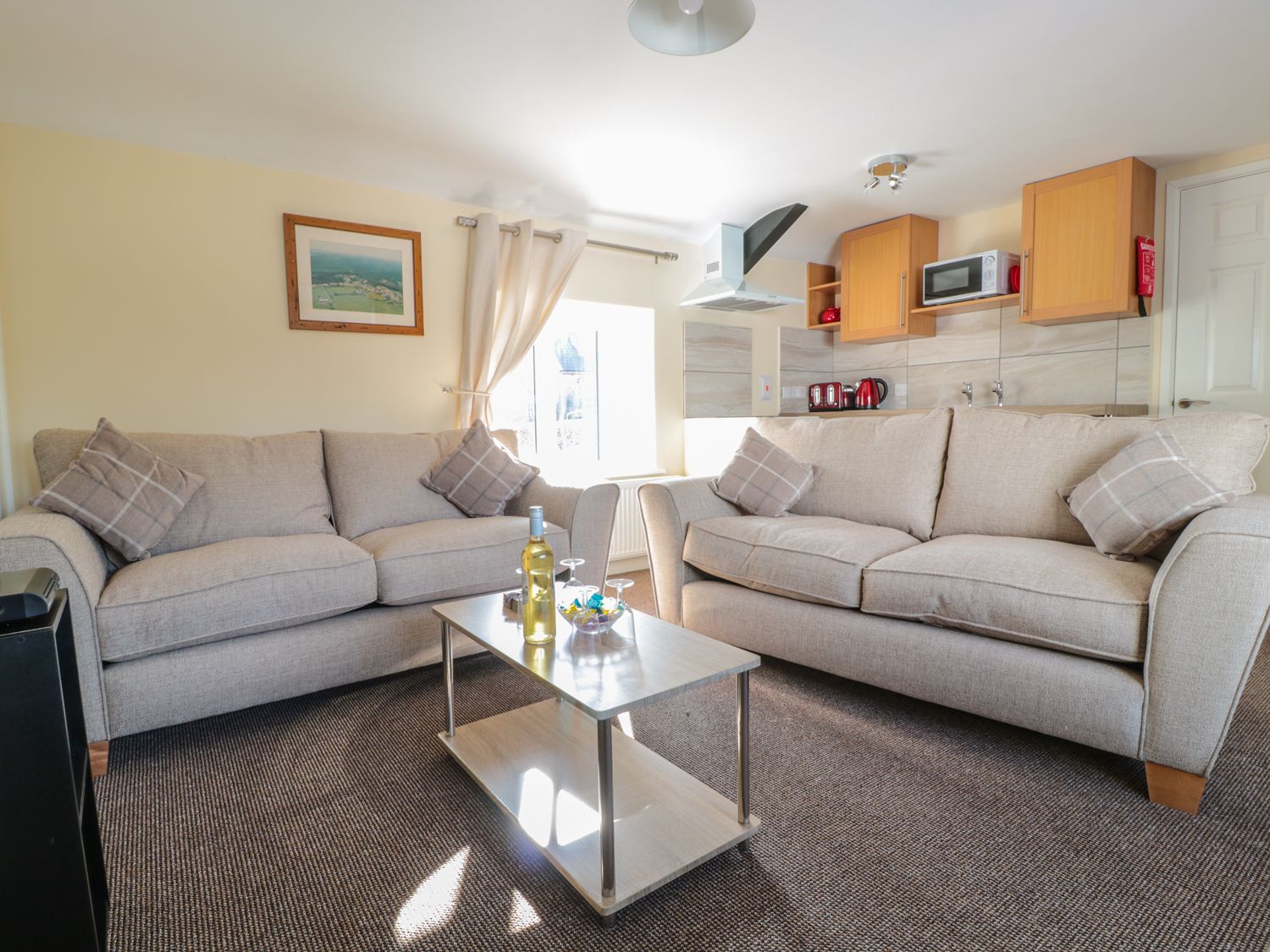 A living room with two sofas a coffee table with wine and glasses and a kitchen area at Brewery Lodge in Blakeney near The Forest of Dean