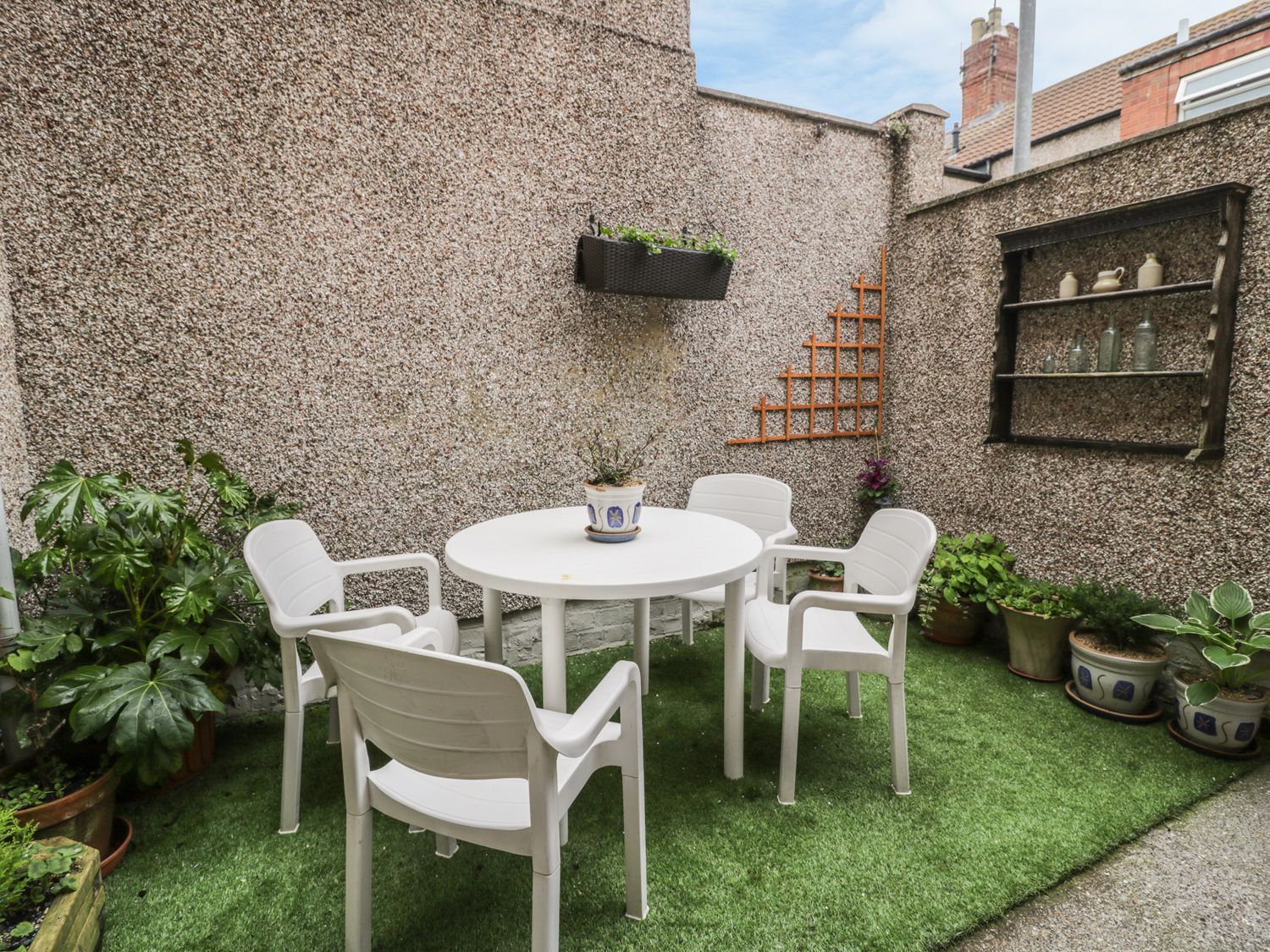 An outdoor patio with a round white table surrounded by four white chairs and various potted plants at Salee Cottage in Newbiggin-by-the-Sea