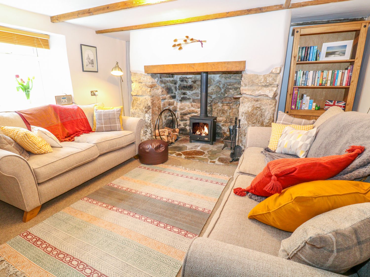 A living room with two sofas a stone fireplace with a wood burning stove a bookshelf and a rug at Blue Anchor in Fraddon