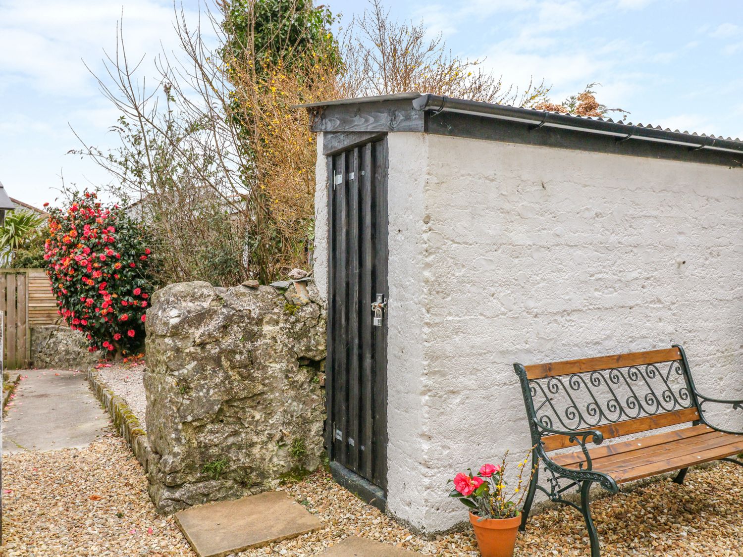 An outdoor bench next to a white shed with a black door and a potted plant in a garden at Blue Anchor in Fraddon