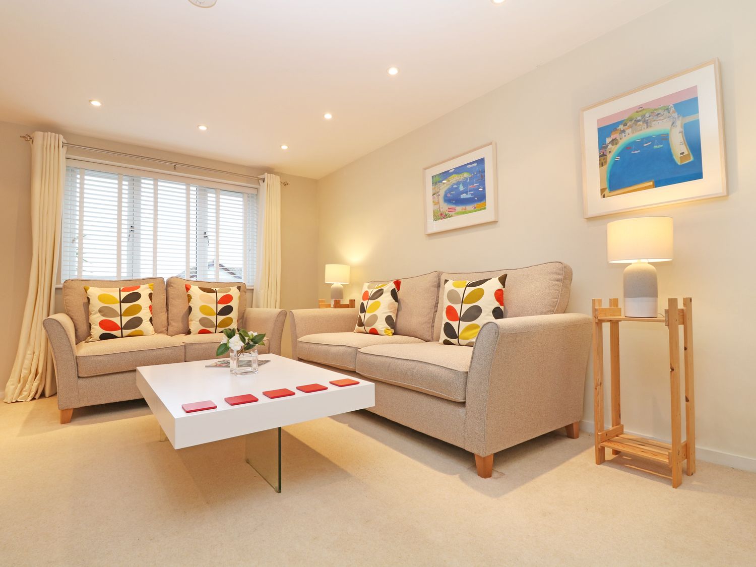 A living room with two beige sofas with patterned cushions a white coffee table and two framed pictures on the wall at Chy Kerris Carbis Bay