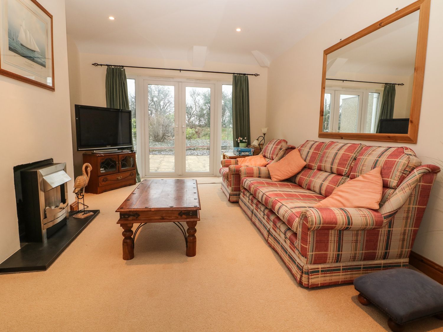 A living room with a plaid sofa and armchair a wooden coffee table a television on a stand and glass doors at Bryn Lleuddad in Sarn Meyllteyrn