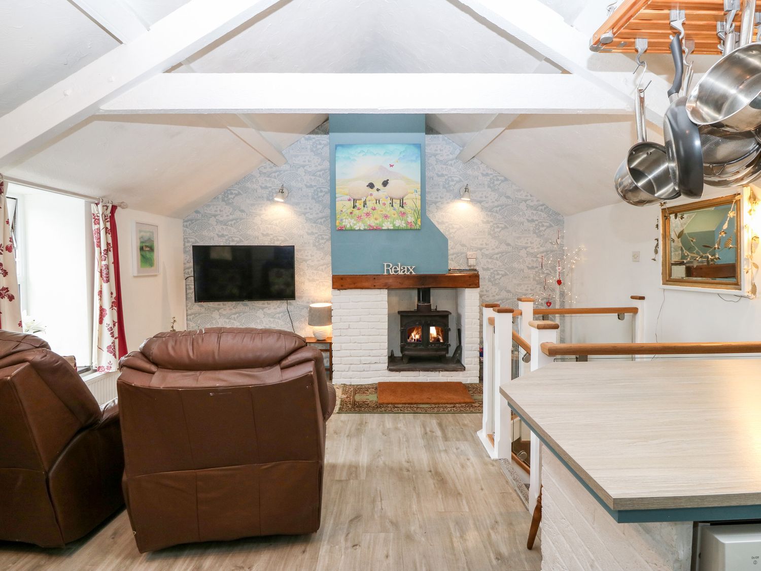 A living room with a fireplace two brown leather armchairs a wall-mounted television and a kitchen counter at Hafod in Y Felinheli