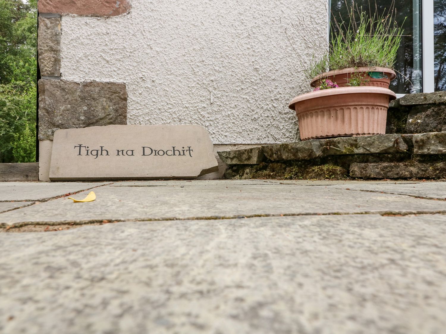 A stone sign with Tigh na Drochit next to a building wall and two flower pots on a stone platform at Tigh Na Drochit in Garve