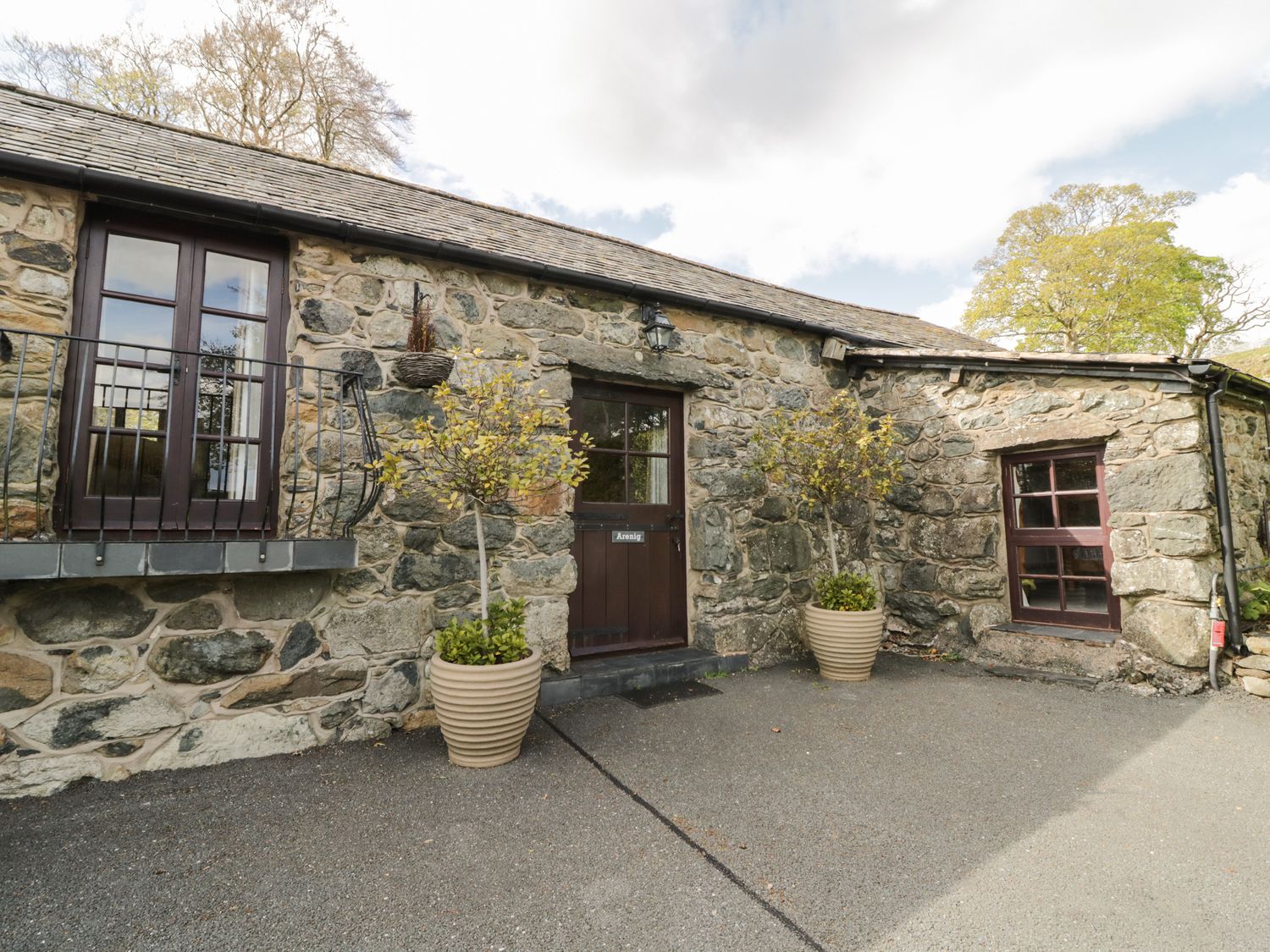 Exterior view of a stone building with two potted plants flanking a wooden door and two windows at Cyffdy Cottage - Arenig Parc near Bala