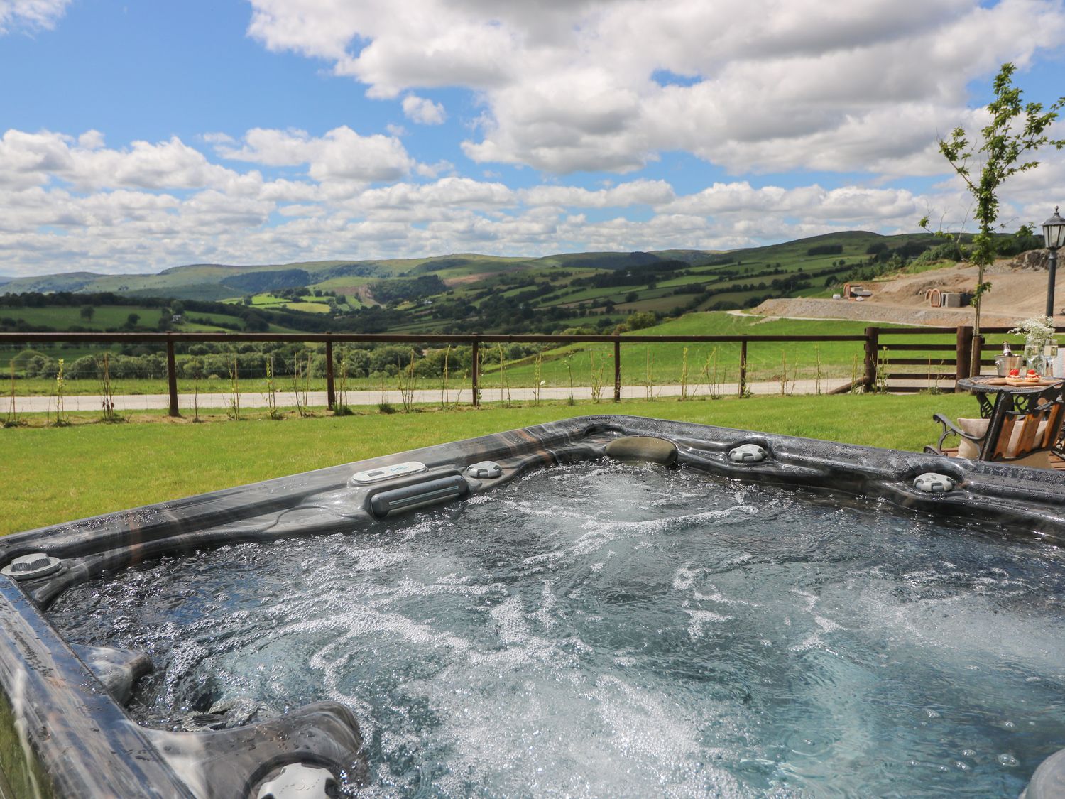 An outdoor hot tub with bubbles overlooking green hills and a partly cloudy sky at Shepherd's View in Rhayader