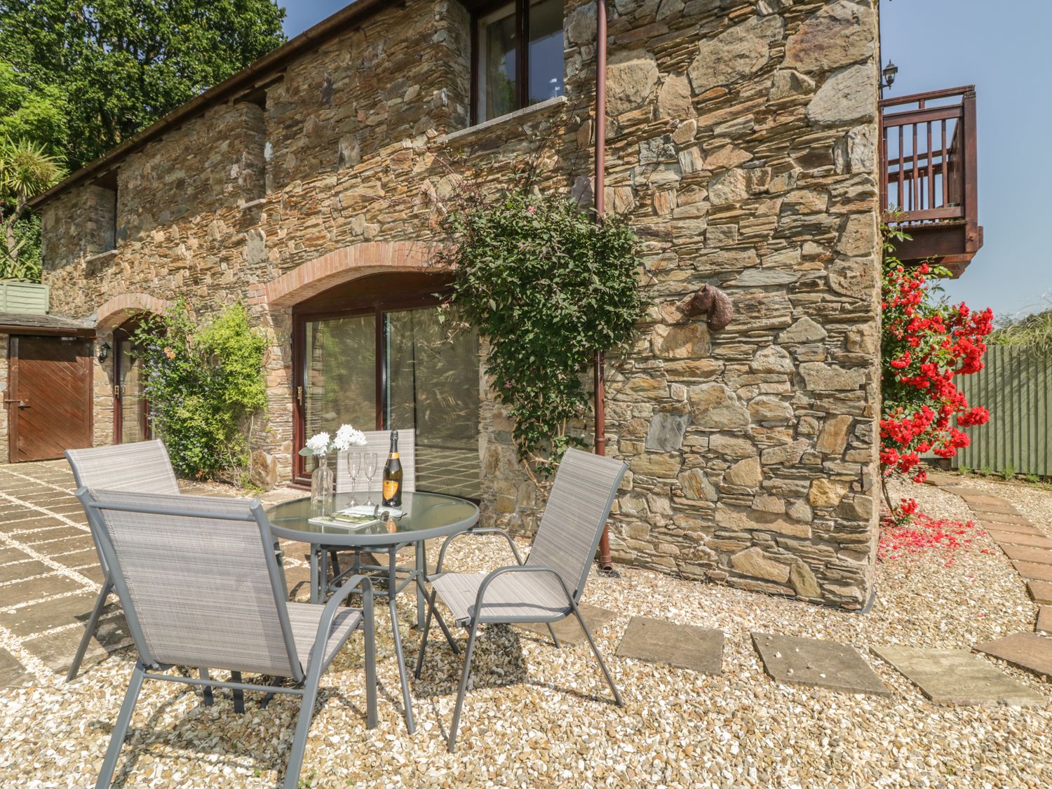 Outdoor patio area with glass table and four chairs by a stone house at Bearscombe in Modbury