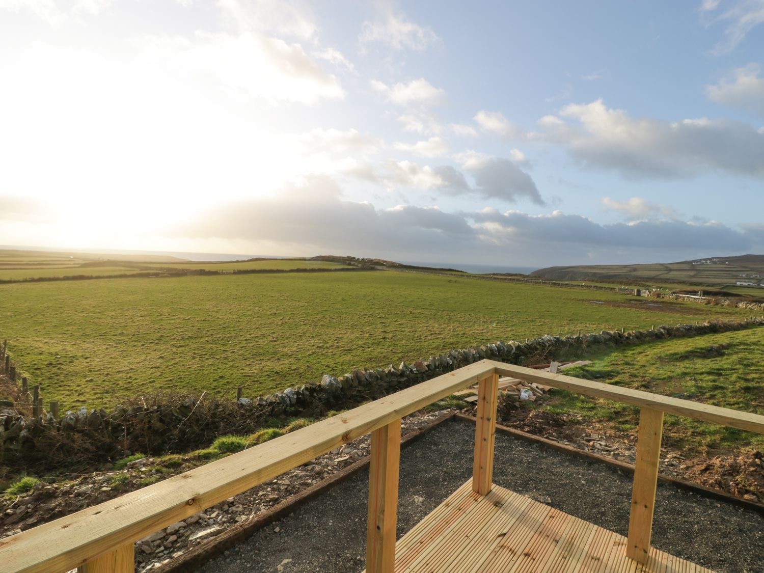 A wooden deck overlooking a grassy field with stone fences under a cloudy sky at Cysgod y Bugail in Holyhead