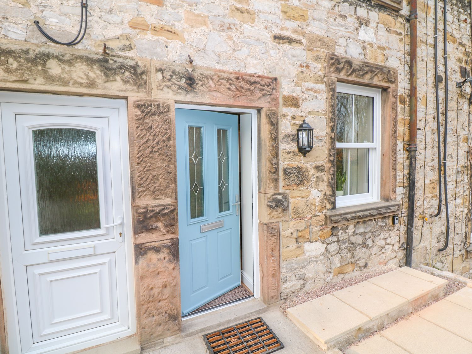 An exterior view of a stone building with a blue front door slightly open and a white door next to it at Wyebrow Cottage in Bakewell