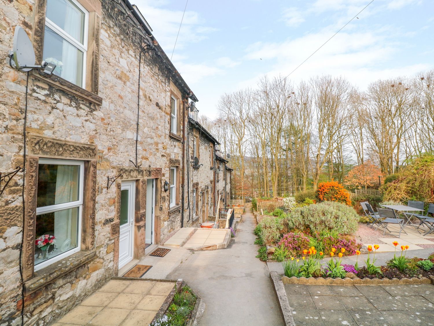 A stone cottage with white doors and windows next to a garden with flowers and outdoor seating at Wyebrow Cottage in Bakewell