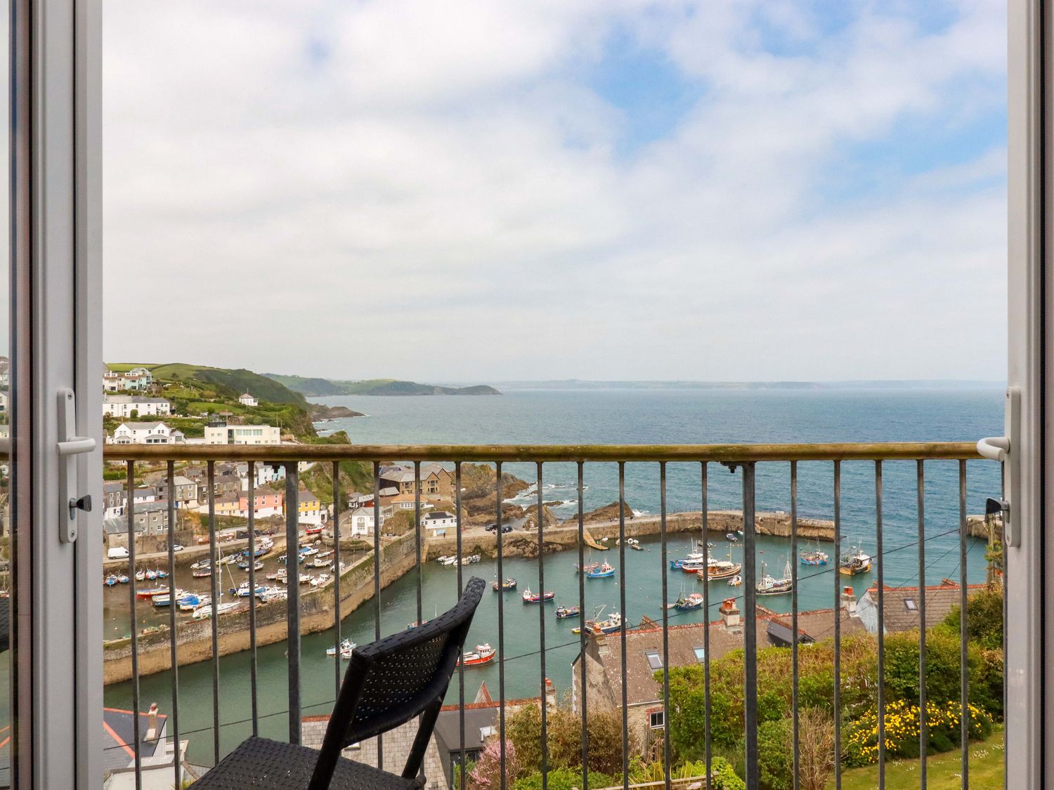 View of a harbor with boats and houses from a balcony with railing and a black chair at Pink House in Mevagissey