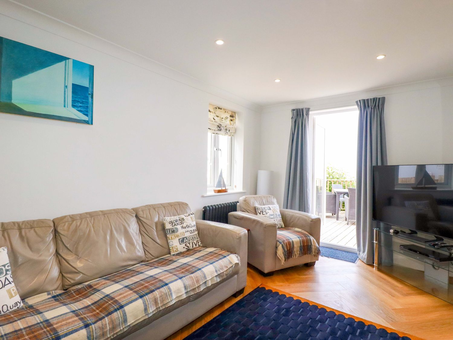 A living room with beige sofas a television and an open door leading to an outdoor seating area at Pink House in Mevagissey