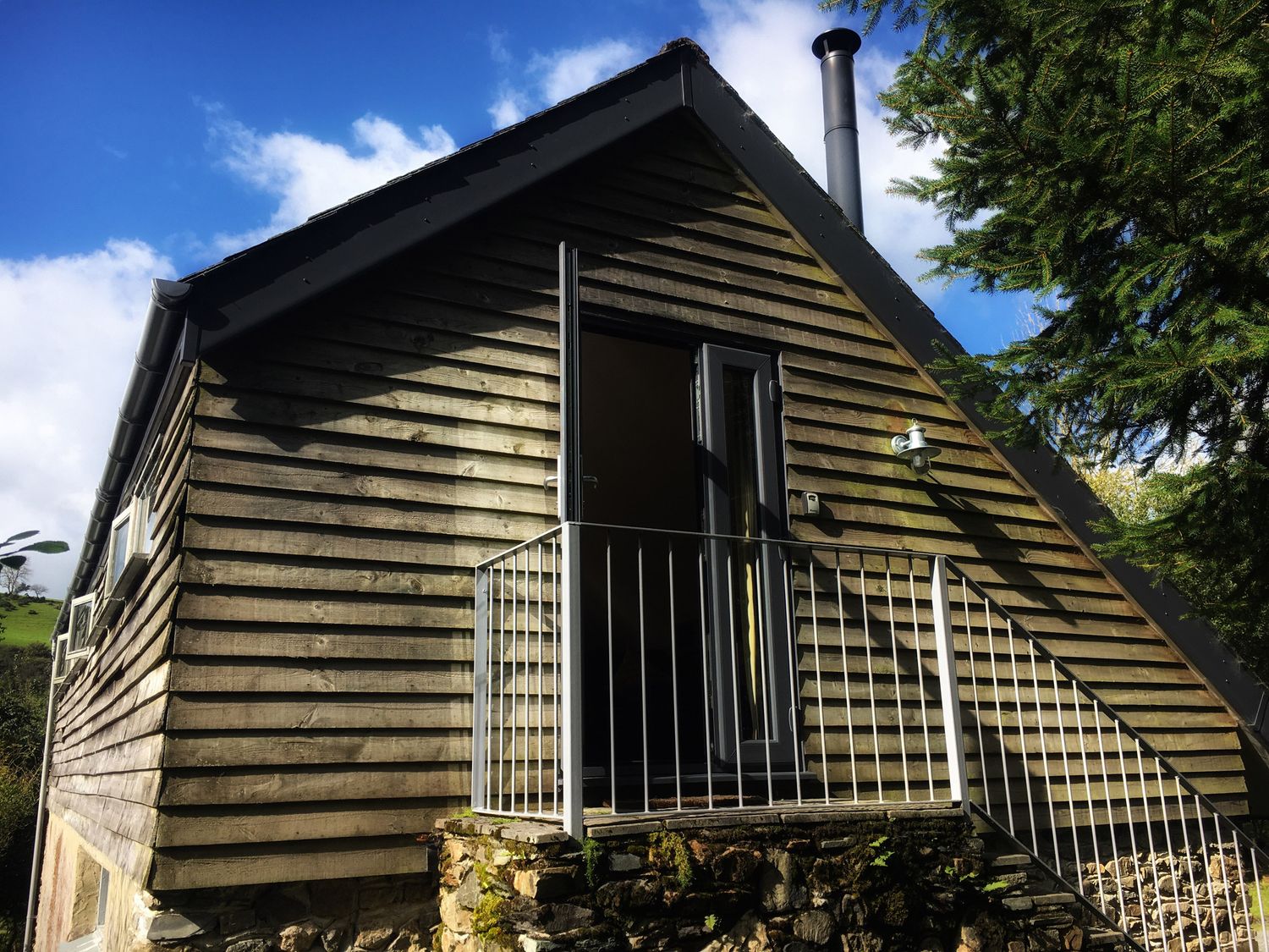 A wooden exterior cabin with a small balcony and metal railing at The Linhay in Lydford