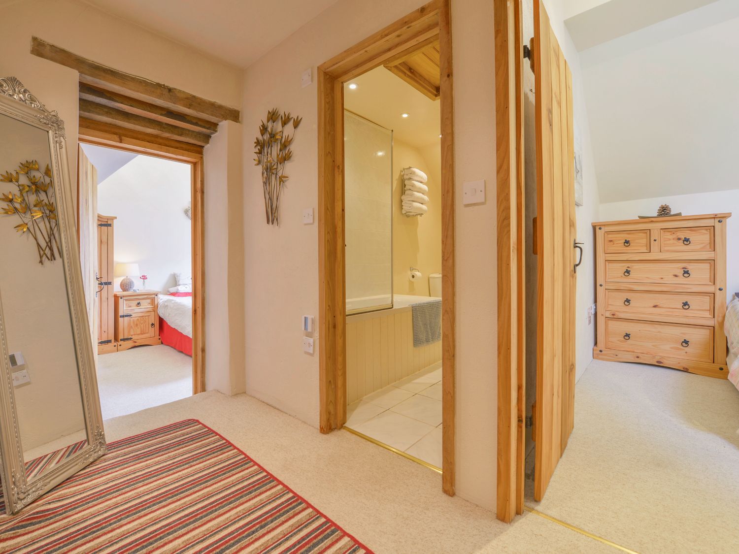 A hallway with a striped rug and mirror leading to a bedroom and bathroom at The Bolthole in Throwleigh near Chagford