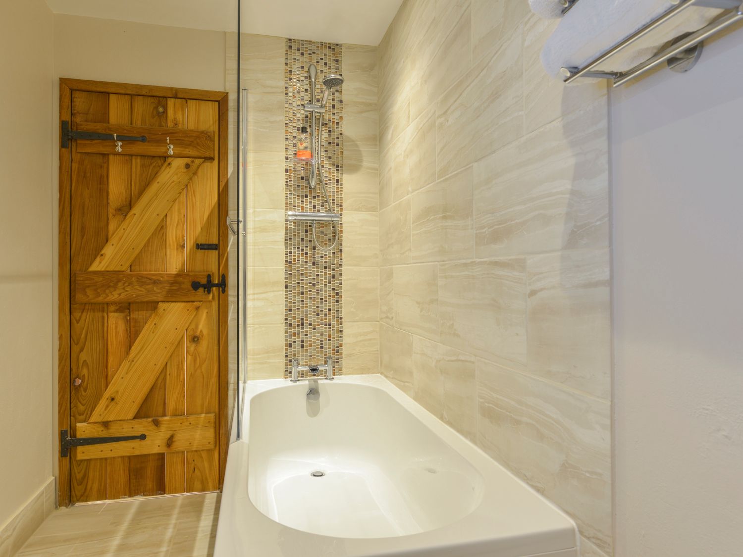 A bathroom with a bathtub a tiled wall a wooden door and a towel rack at The Bolthole in Throwleigh near Chagford