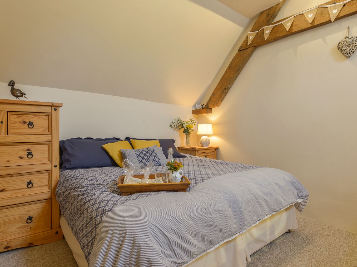A bedroom with a bed with patterned bedding and pillows two wooden bedside tables a lamp and a wooden chest of drawers at The Bolthole in Throwleigh near Chagford