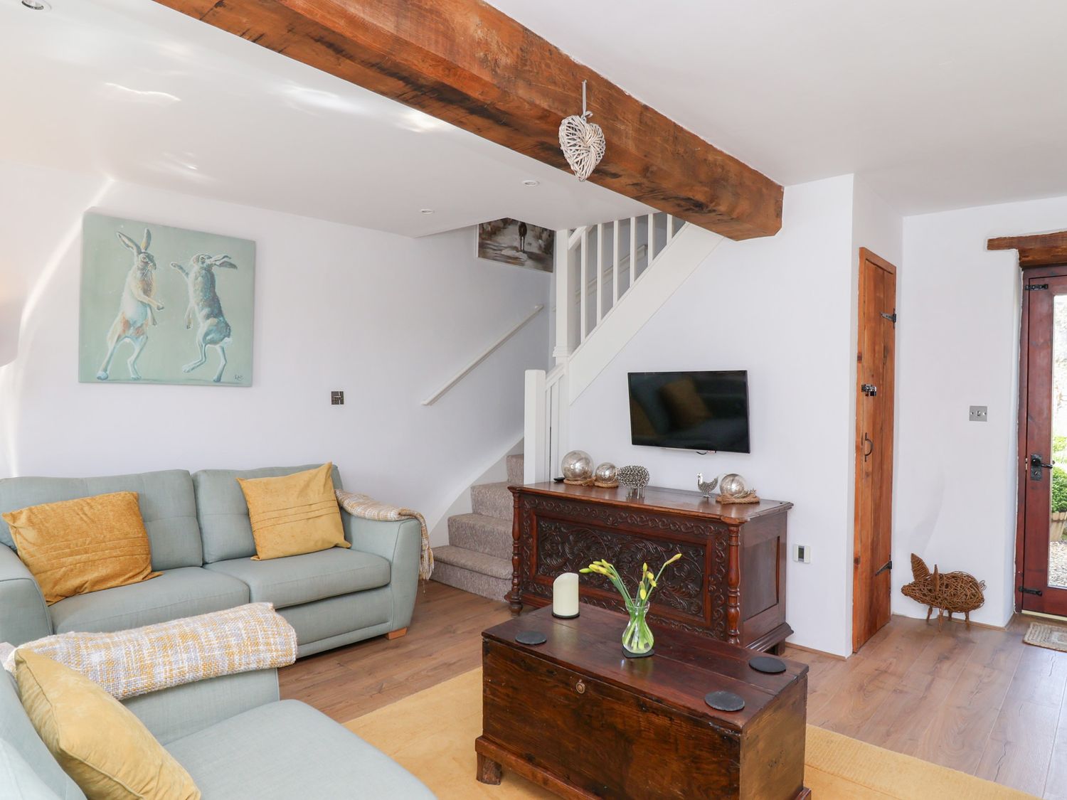 A living room with sofas cushions a wooden chest a television on a carved wooden sideboard and stairs at The Bolthole in Throwleigh near Chagford