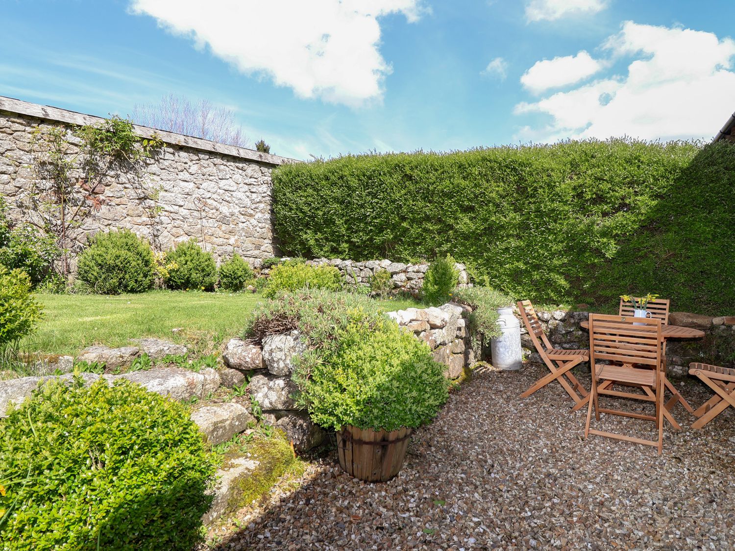 An outdoor garden area with stone walls wooden table and chairs and green bushes at The Bolthole in Throwleigh near Chagford