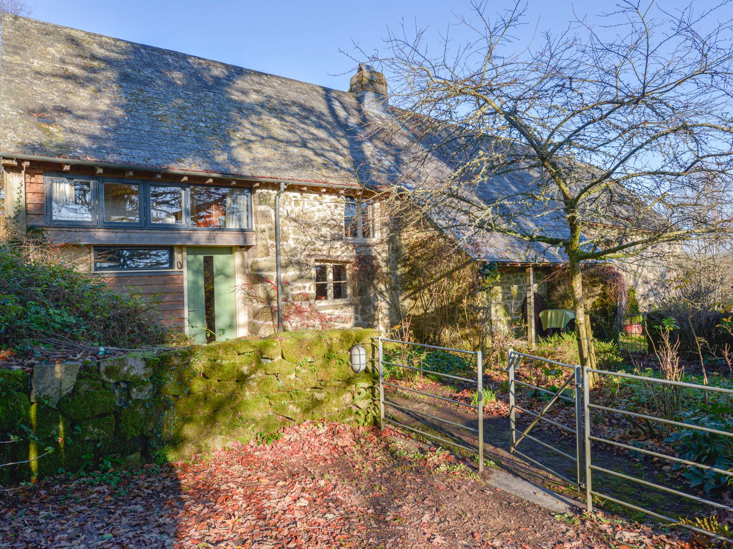 Stone cottage with moss covered wall metal gate and leaf covered ground at The Bakehouse in Gidleigh