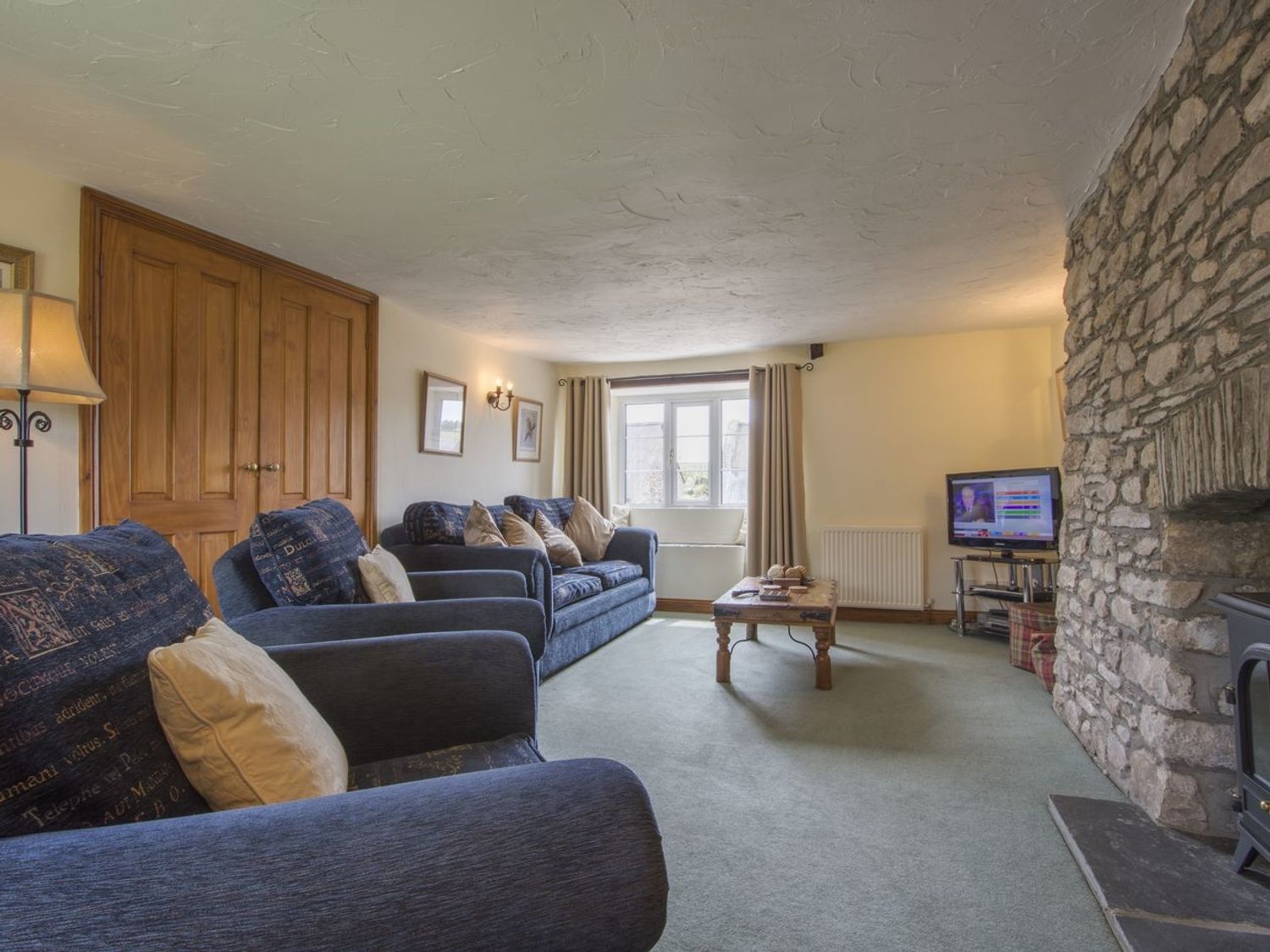 A living room with blue sofas a wooden coffee table a stone fireplace and a television at Owls Roost in Combe Martin