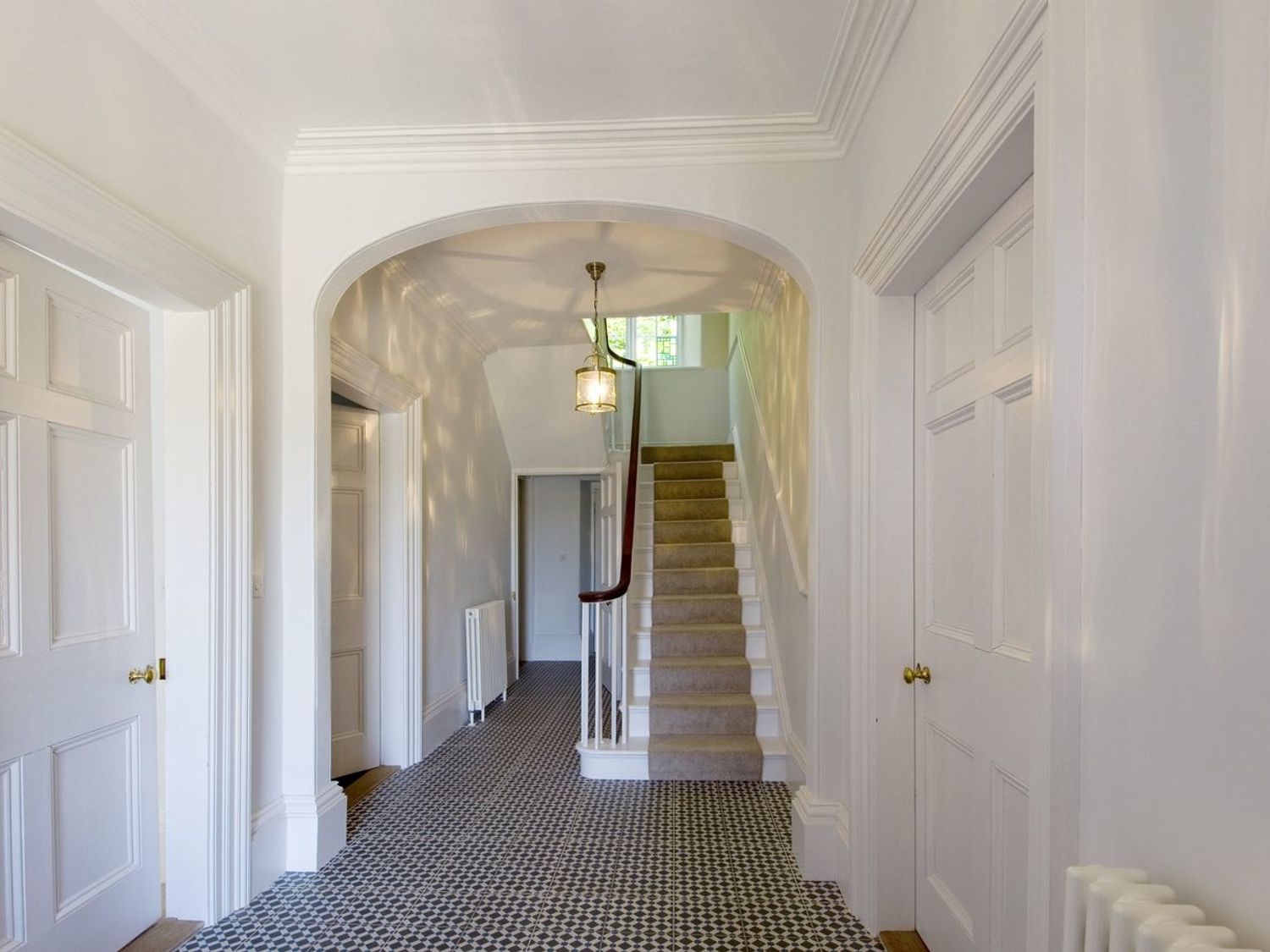 A hallway with patterned floor tiles, white walls, an arched doorway, and a staircase at The Mount in Dulverton