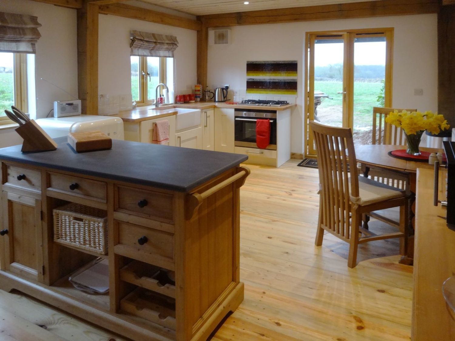 A kitchen with wooden cabinets an island dining table with chairs and flowers on the table at The Woodshed in Upton Pyne