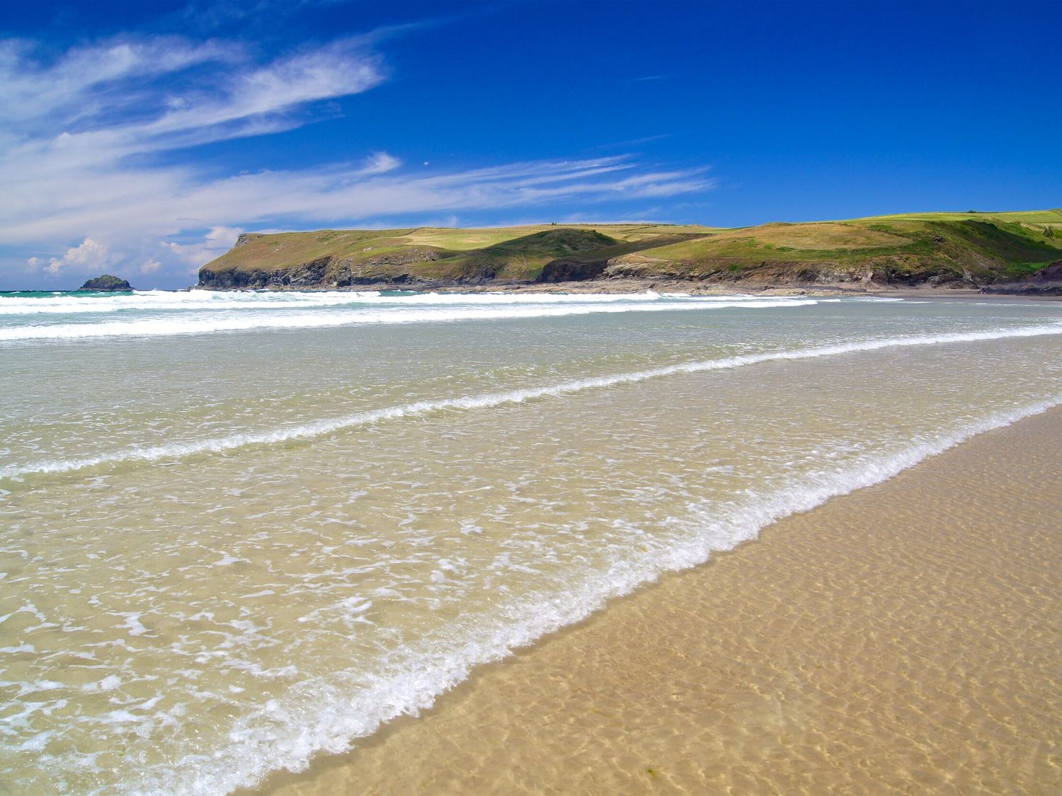 A sandy beach with gentle waves and a grassy cliff in the background at Chapel Cottage in Welcombe