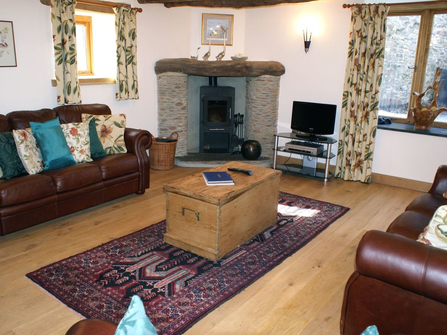 A living room with brown leather sofas a wooden chest coffee table a fireplace and a television at The Hay Barn in Halwell