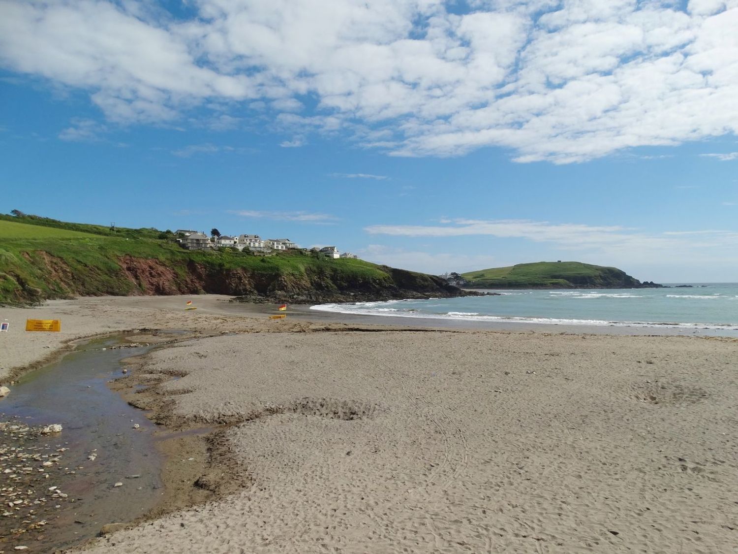 A sandy beach with a small stream flowing into the sea and houses on cliffs in the background at 5 Beachdown in Challaborough near Bigbury-on-sea