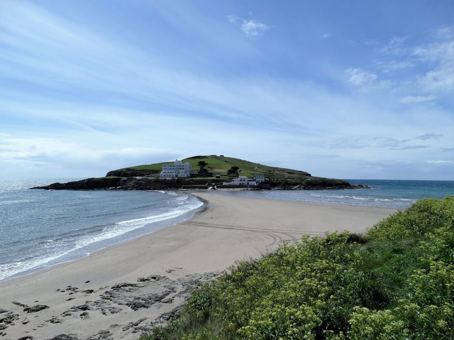 A sandy beach leading to a grassy hill with buildings near the coastline at 5 Beachdown in Challaborough near Bigbury-on-sea