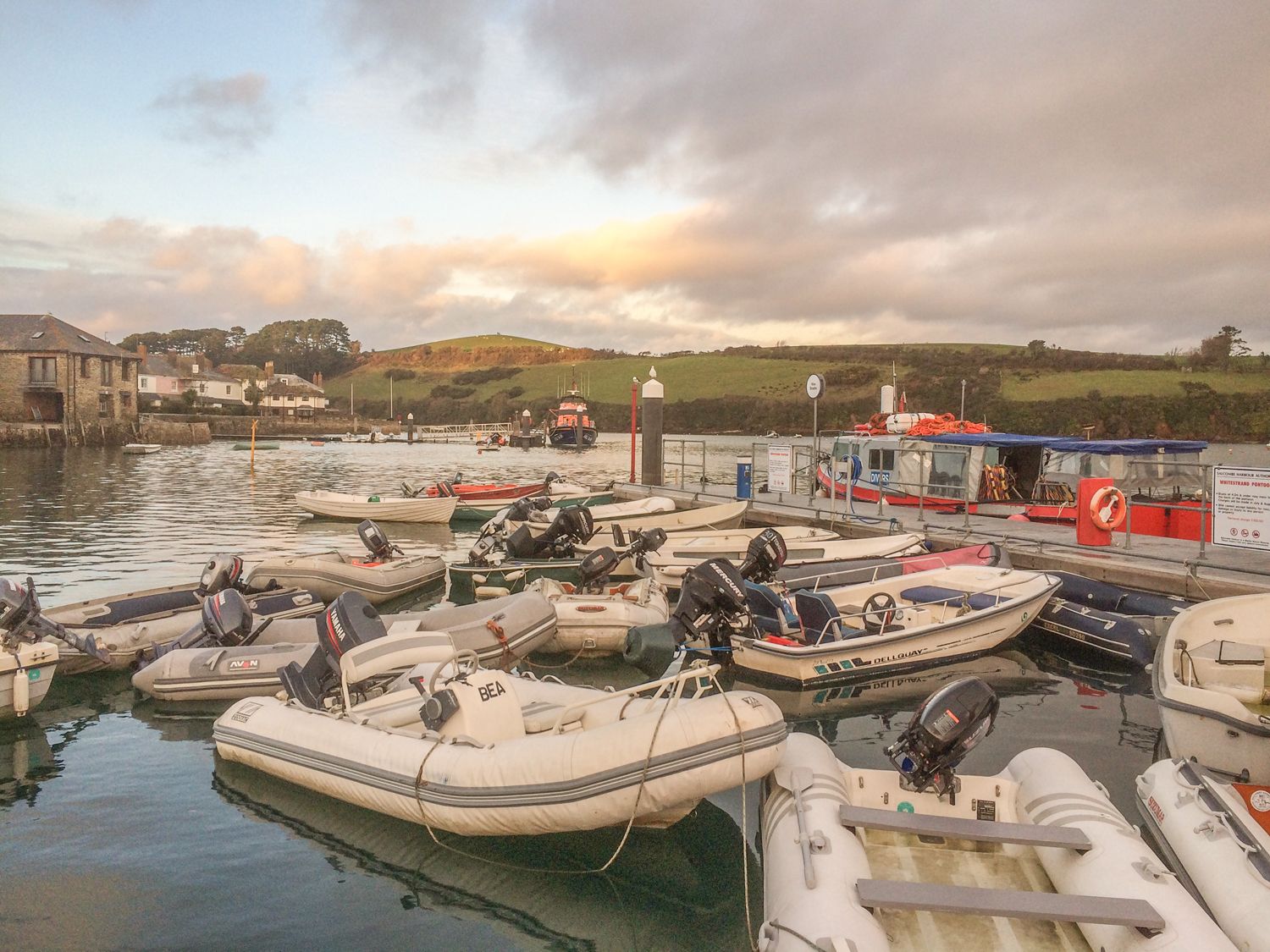 Several small motorboats docked in a harbor with buildings and green hills in the background at Orchard View in Kellaton near Hallsands