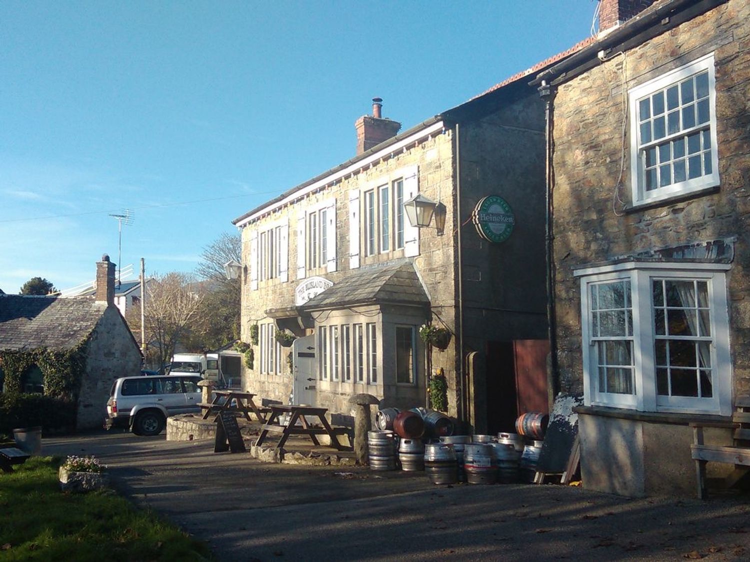 Exterior of a stone building with picnic tables barrels and a parked car at Higher Tumrose in Blisland