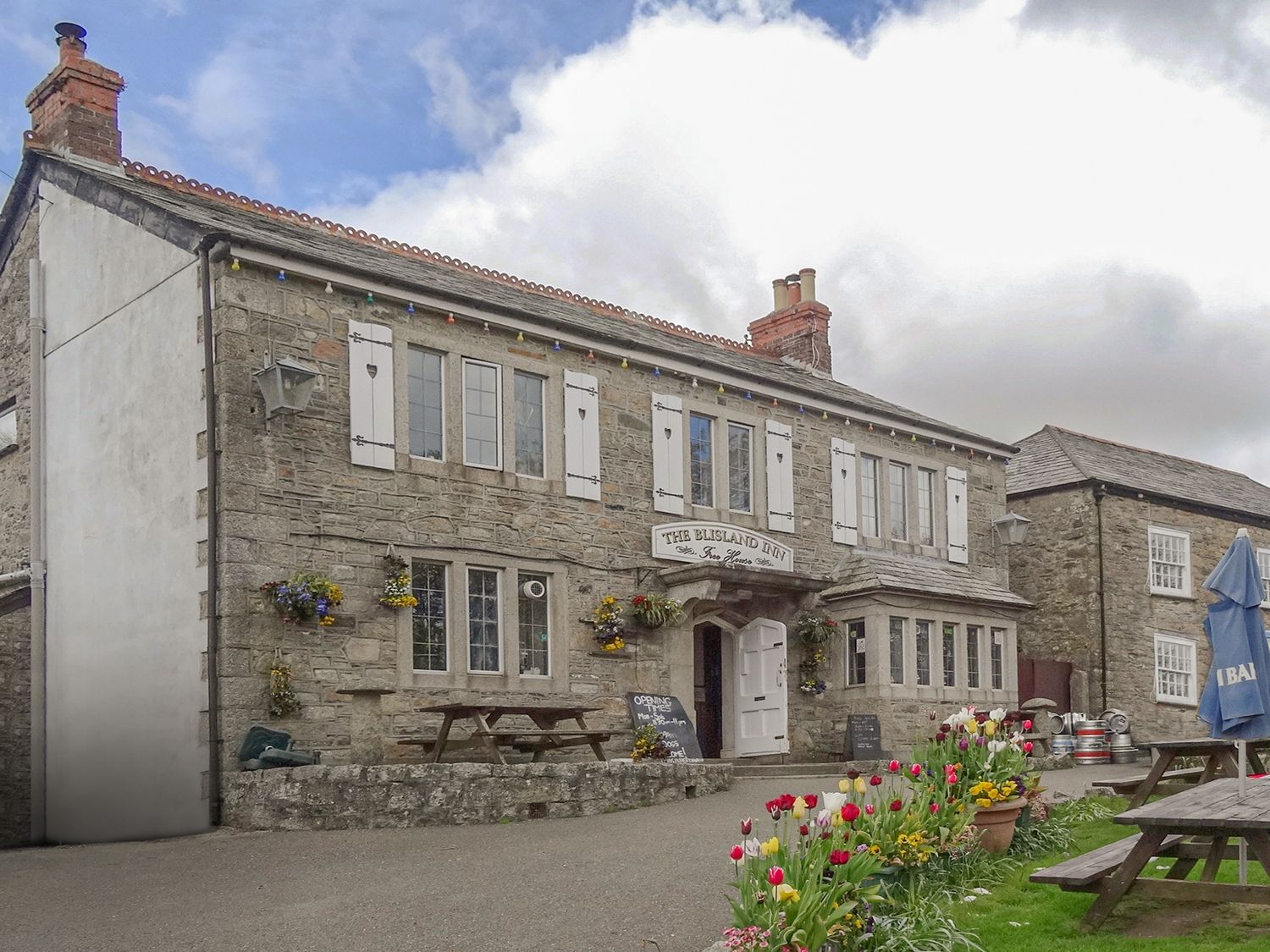 A stone building with white shutters and flower beds outside at The Blisland Inn in Blisland