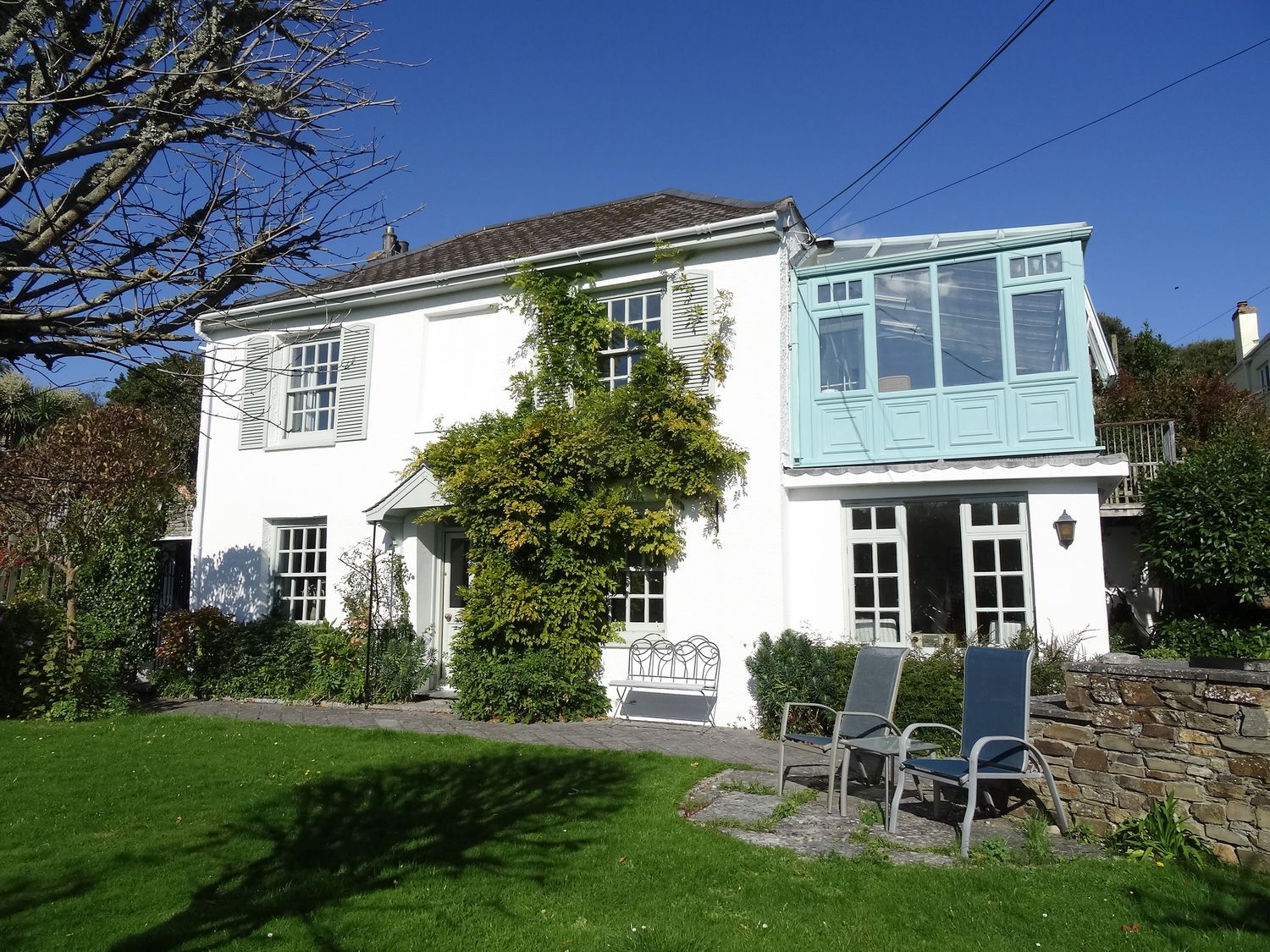 A white two-story house with a garden bench and two outdoor chairs in a green lawn at Mount Pleasant in Padstow