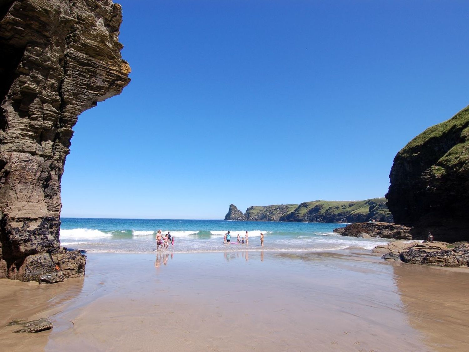 A beach with people near the water and rocky cliffs on both sides at Orchard Lodge in Boscastle