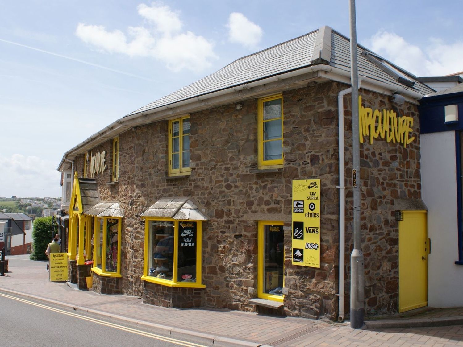 A stone building with yellow window frames and signage on a street at The Workshop in Bude