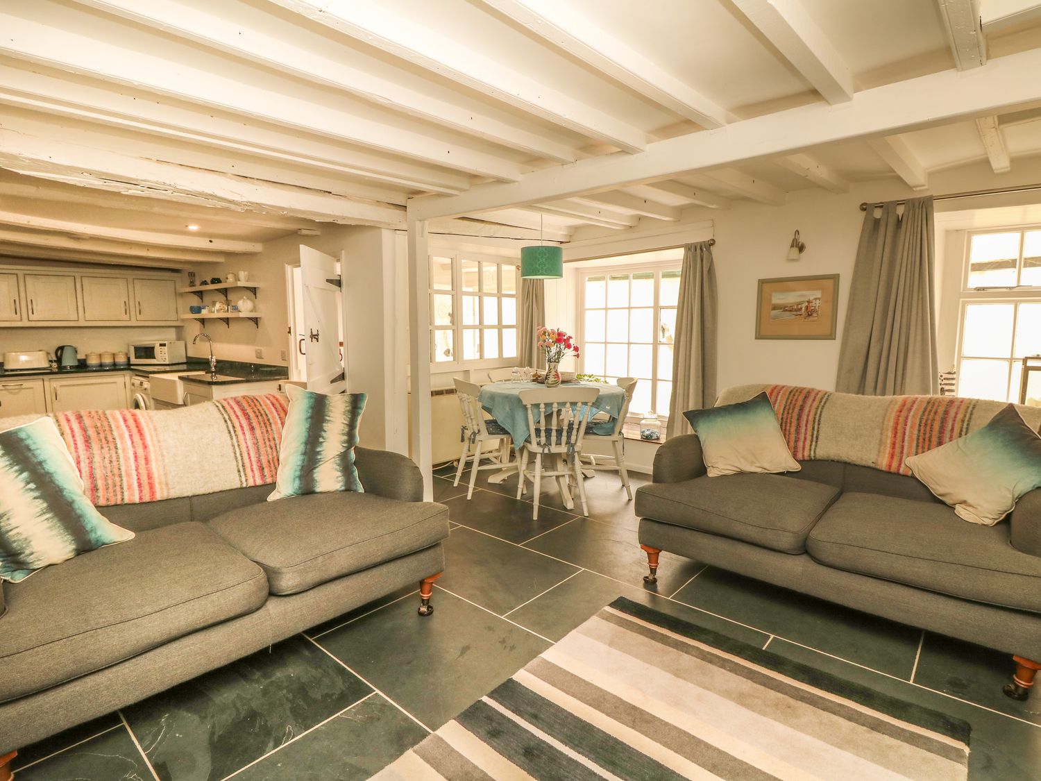 A living room with two grey sofas and a dining table with chairs near windows at Cousham Cottage in Kingsand And Cawsand