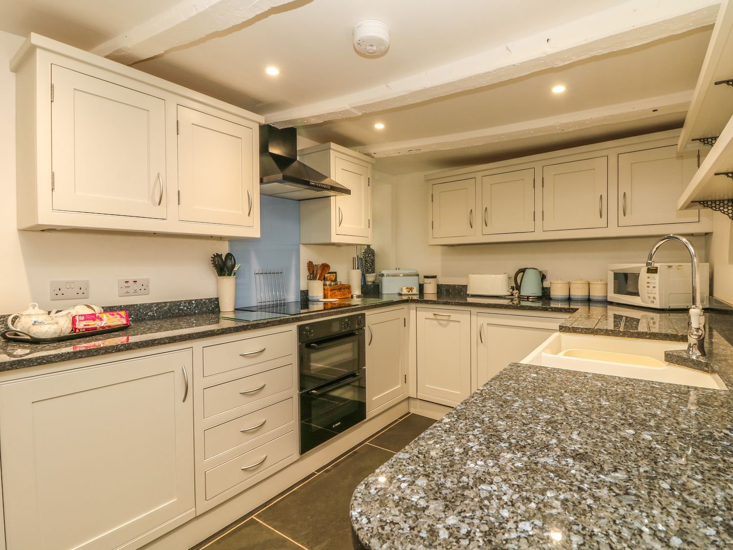 A kitchen with white cabinets black countertop sink microwave oven and various kitchen appliances at Cousham Cottage in Kingsand And Cawsand