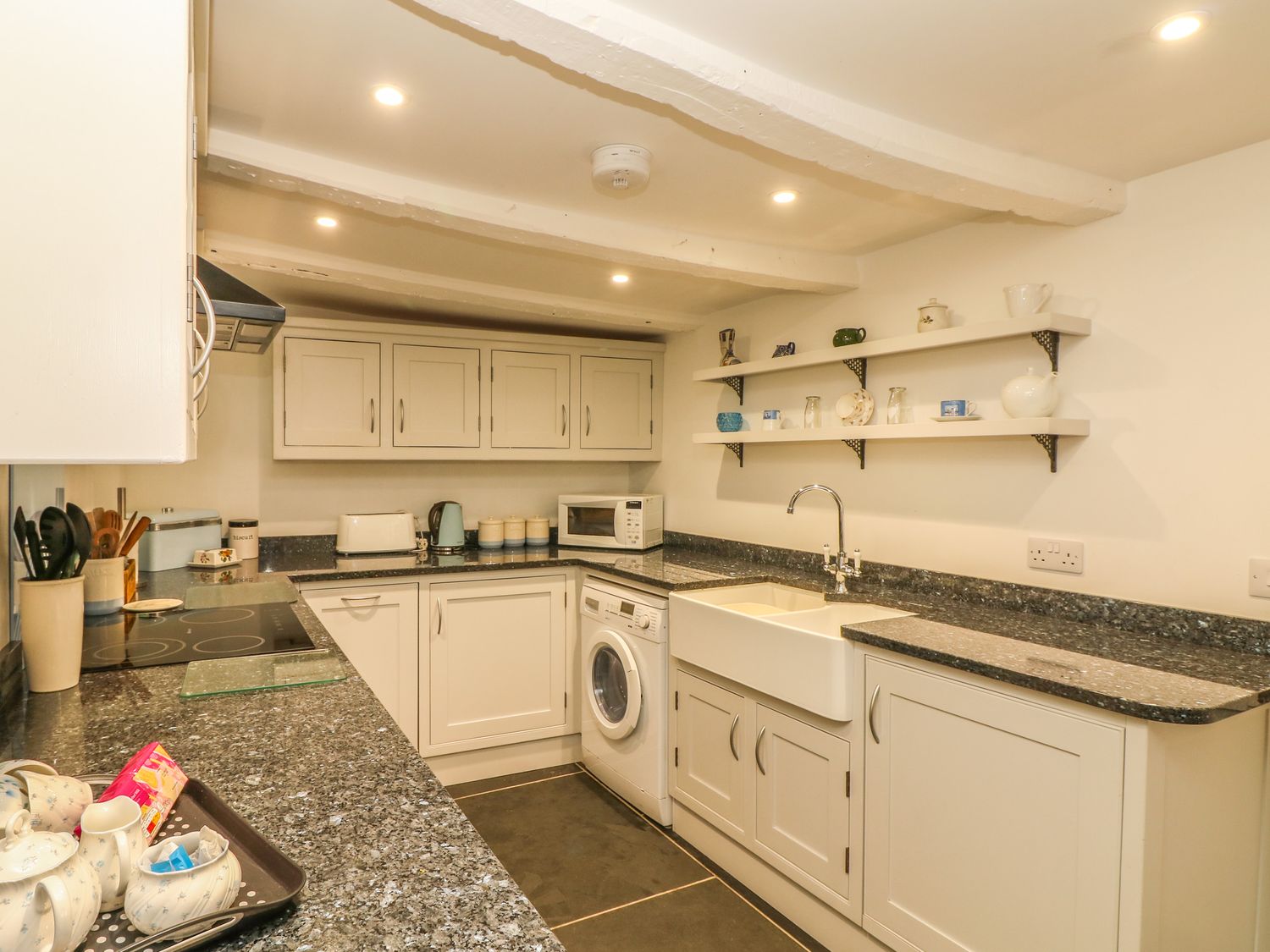 A kitchen with white cabinets a washing machine microwave and shelves with cups at Cousham Cottage in Kingsand And Cawsand