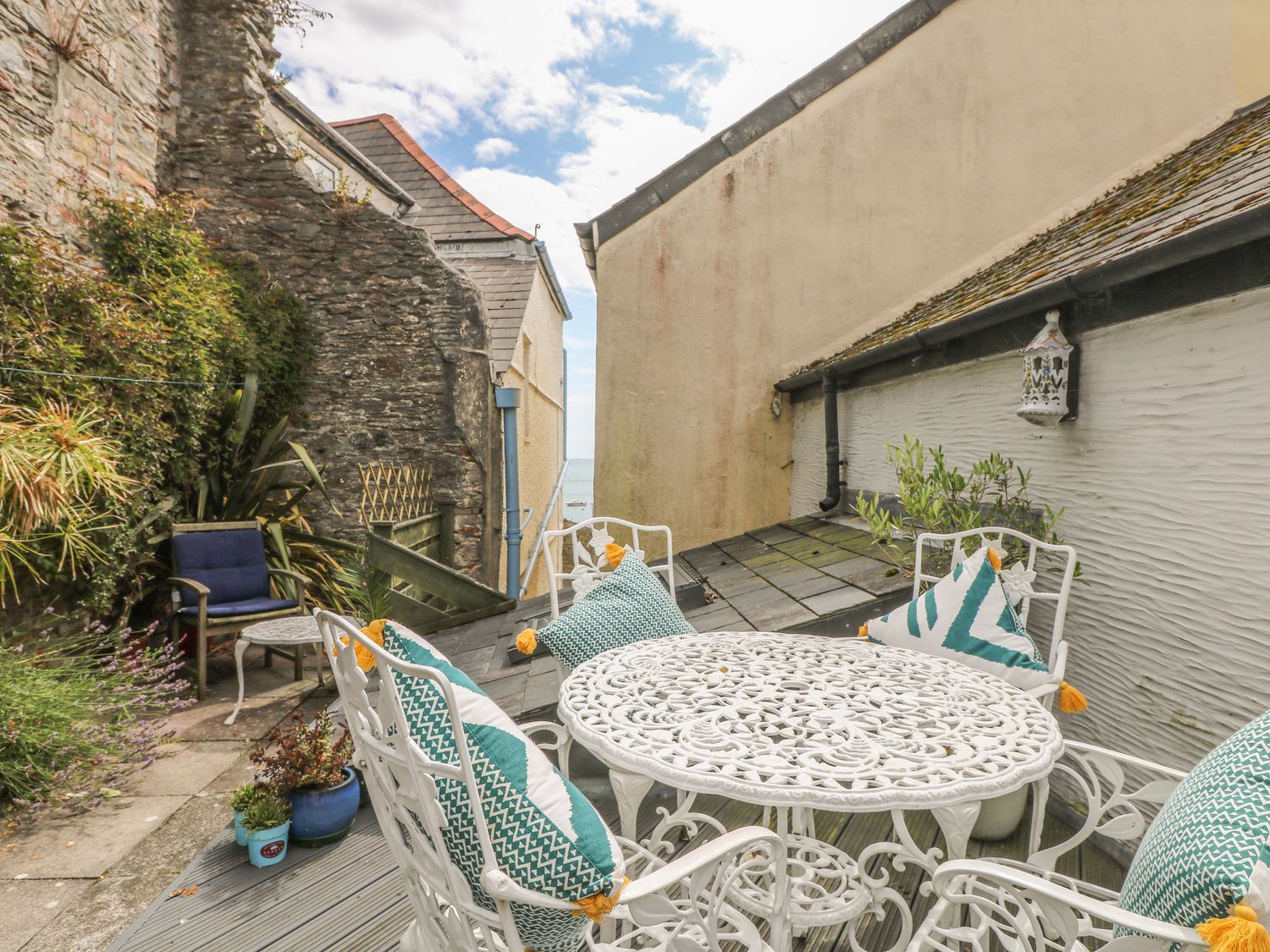 An outdoor patio area with a white metal table and chairs with cushions and plants around at Cousham Cottage in Kingsand And Cawsand
