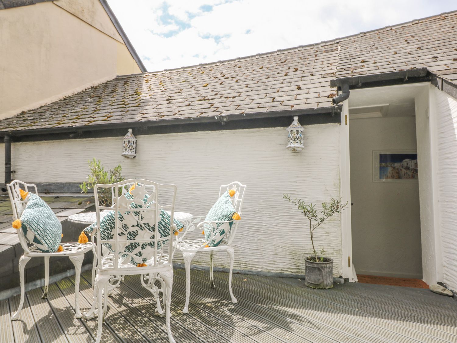 An outdoor patio with white metal chairs and table with cushions on the chairs at Cousham Cottage in Kingsand And Cawsand