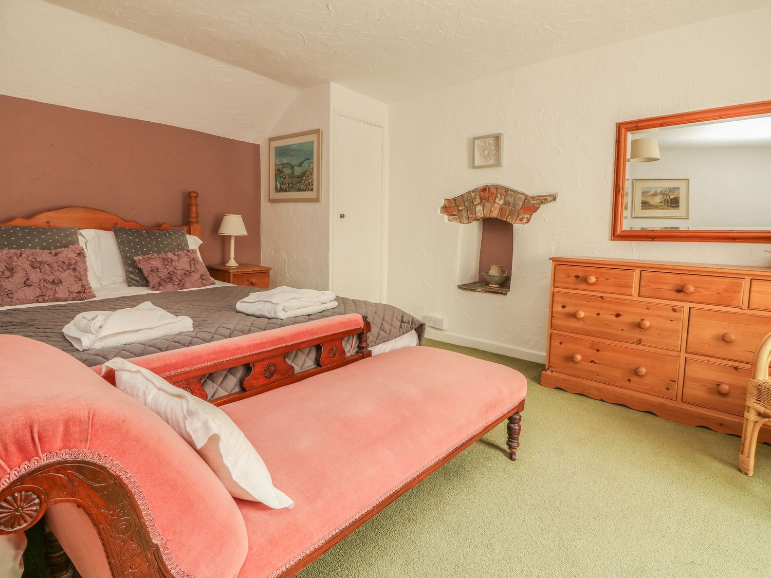 A bedroom with a double bed pink bench wooden dresser and mirror at Cousham Cottage in Kingsand And Cawsand