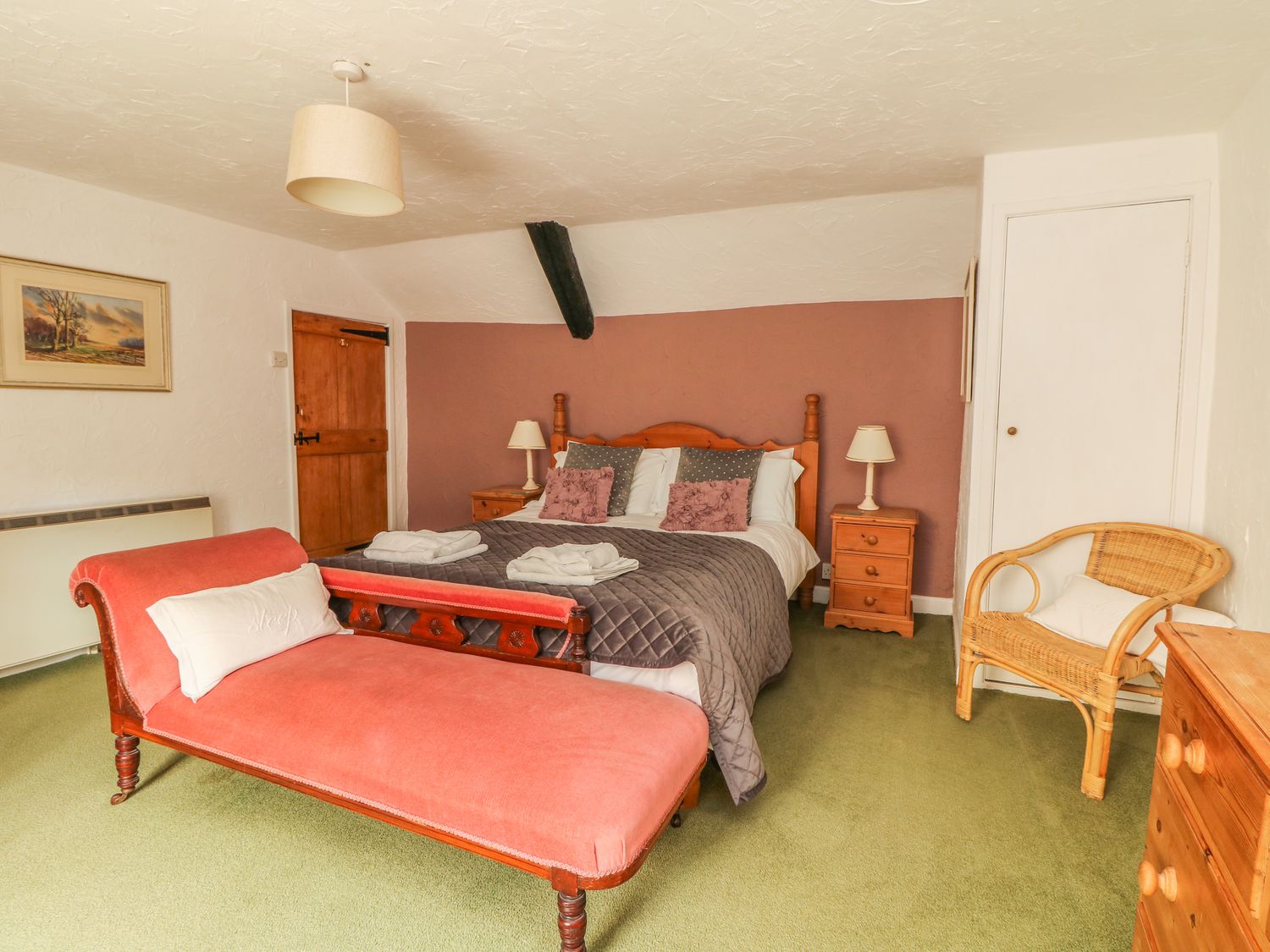 A bedroom with a double bed two bedside tables with lamps a wooden door a wicker chair and a pink chaise lounge at Cousham Cottage in Kingsand And Cawsand