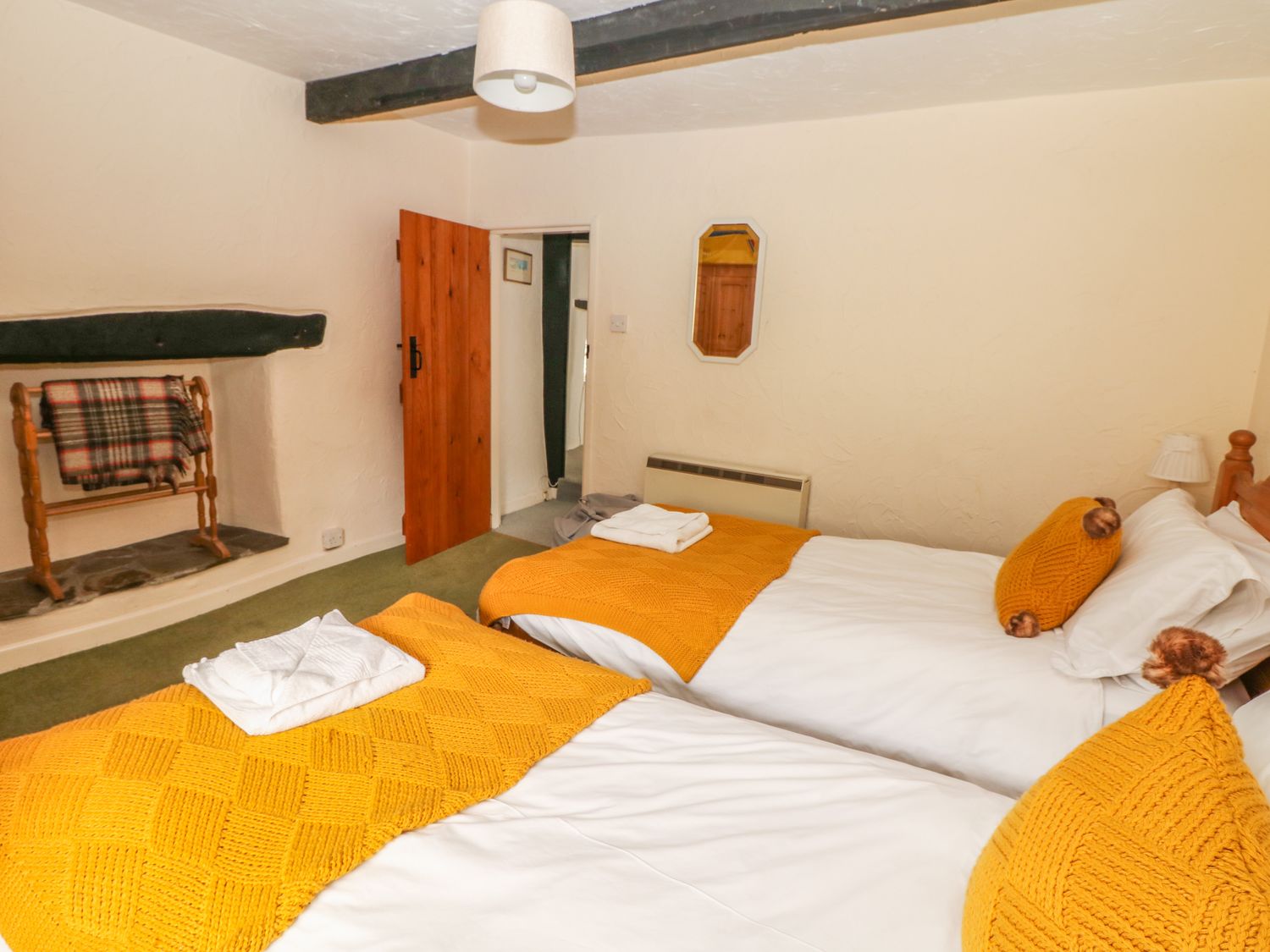 A bedroom with two single beds with yellow blankets and pillows a wooden door and a tartan blanket on a stand at Cousham Cottage in Kingsand And Cawsand