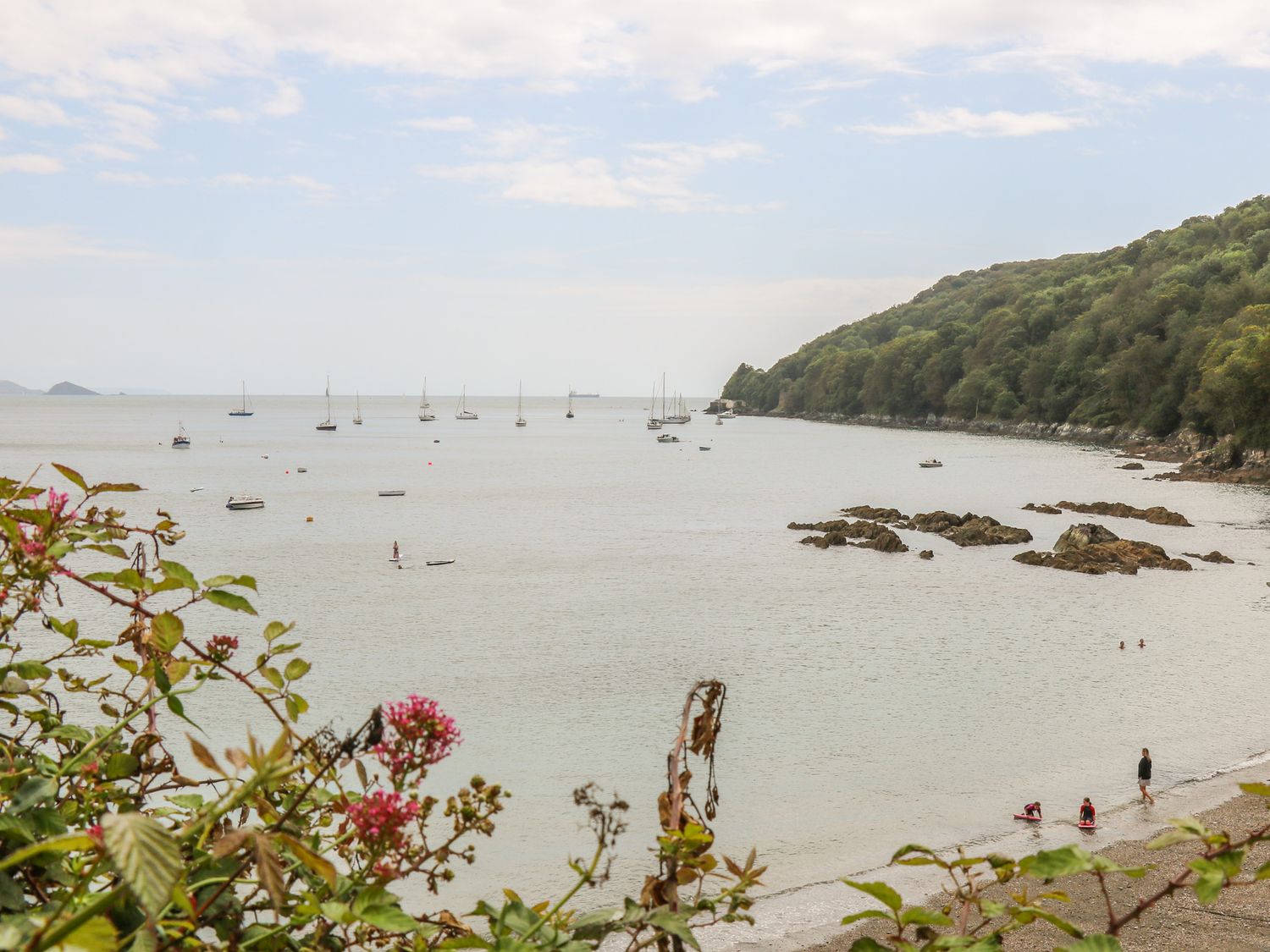 A coastal view with boats on the water a rocky shoreline and people on a beach at Cousham Cottage in Kingsand And Cawsand